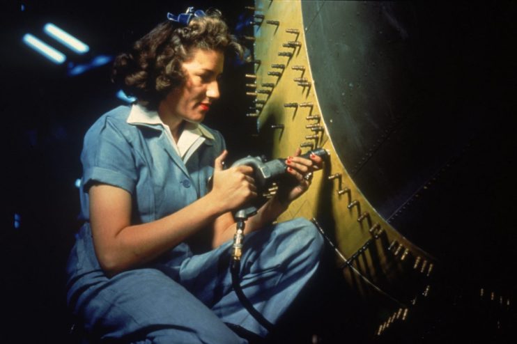 Rosie the Riveter-inspired worker in a factory setting, wearing a blue jumpsuit and red bandana, using a riveting tool.