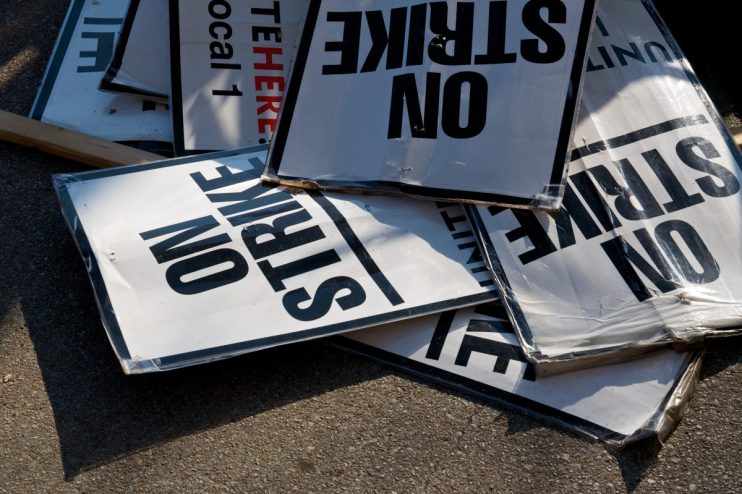 Workers holding signs and banners in a strike action, demanding better working conditions and wages in a public demonstrat...