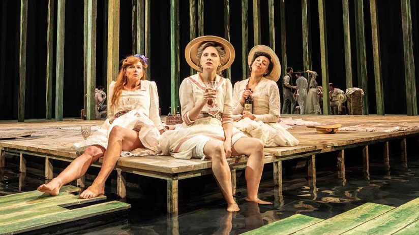 Summerfolk festival attendees enjoying live music outdoors under clear skies with vibrant festival decorations in the back...