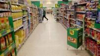 Busy supermarket aisle with shoppers browsing shelves stocked with groceries and essential goods