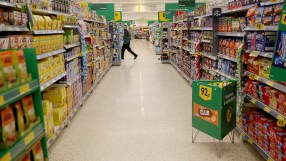 Busy supermarket aisle with shoppers browsing shelves stocked with groceries and essential goods