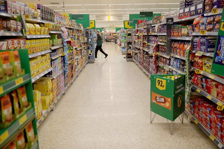 Busy supermarket aisle with shoppers browsing shelves stocked with groceries and essential goods