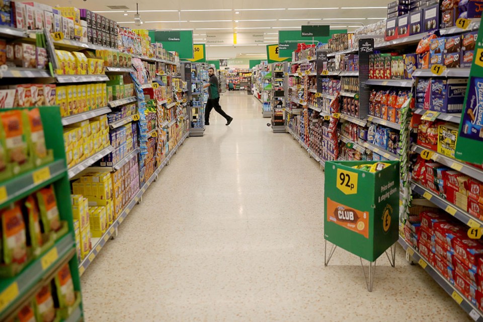 Busy supermarket aisle with shoppers browsing shelves stocked with groceries and essential goods