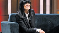 Claudia Winkleman at a press event, wearing a stylish outfit, speaking with journalists, showcasing her iconic fringe hair...