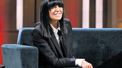 Claudia Winkleman at a press event, wearing a stylish outfit, speaking with journalists, showcasing her iconic fringe hair...