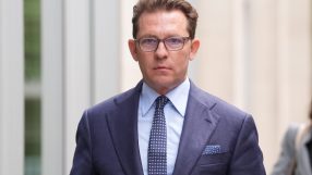 Nick Candy in a business suit attending a corporate event with a backdrop featuring company logos and a crowd of attendees.