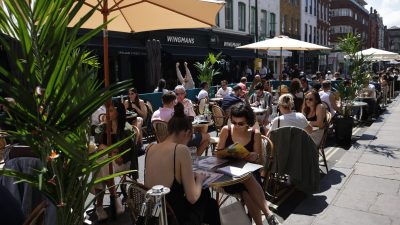 Bustling Soho street scene with vibrant storefronts, diverse pedestrians, and iconic London architecture under clear skies