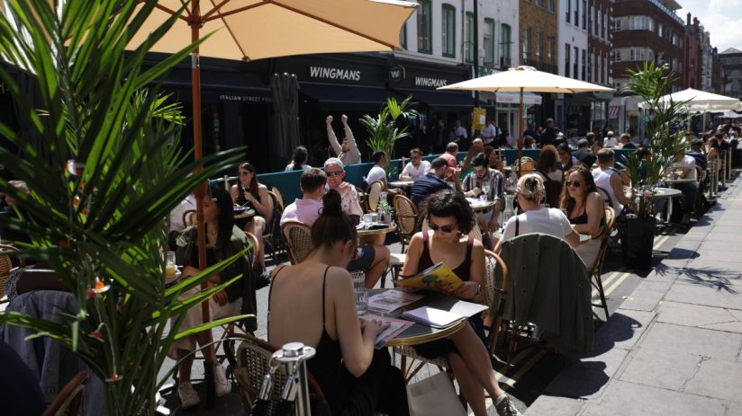 Bustling Soho street scene with vibrant storefronts, diverse pedestrians, and iconic London architecture under clear skies