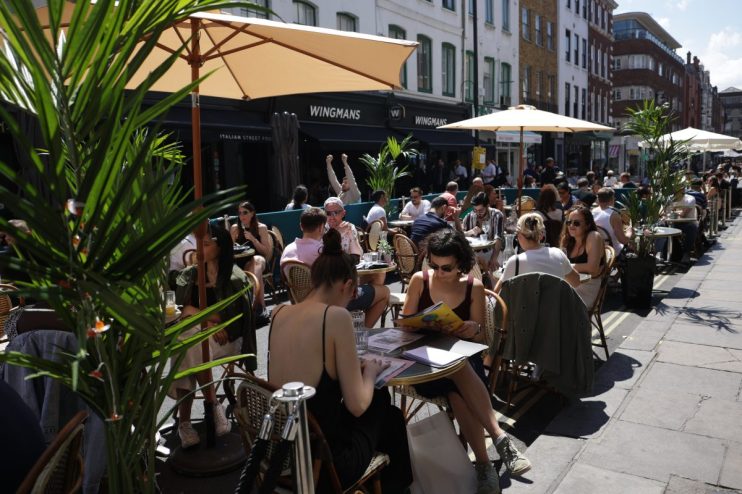 Bustling Soho street scene with vibrant storefronts, diverse pedestrians, and iconic London architecture under clear skies