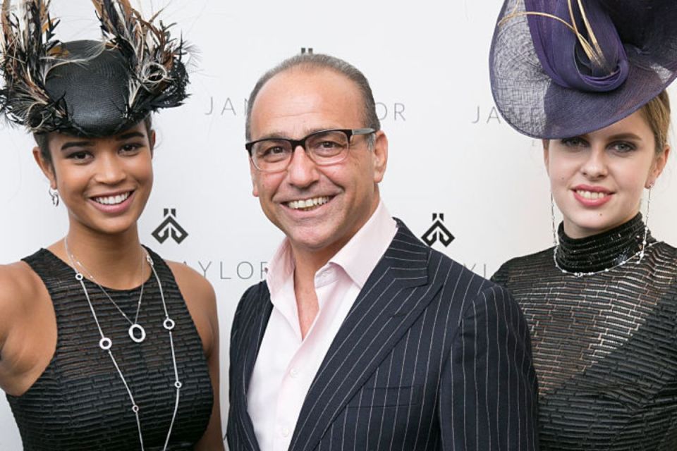 Theo Paphitis in a business setting, wearing a suit, gesturing while engaged in a conversation or presentation.