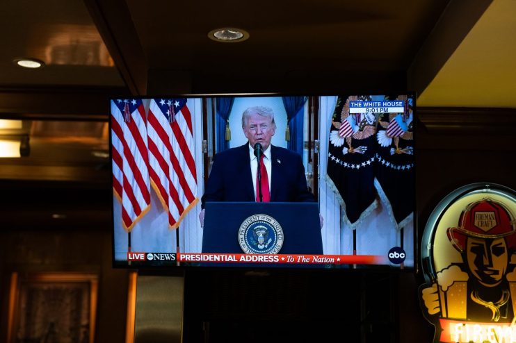 Donald Trump speaking at a press conference with American flags in the background, emphasizing political stance and leader...
