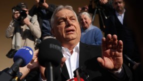 Hungarian Prime Minister Viktor Orban speaking at a press conference, gesturing with his hands, with a serious expression.