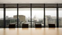 Modern boardroom setup with large conference table, executive chairs, and digital presentation screen in a corporate offic...