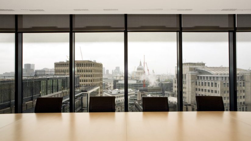 Modern boardroom setup with large conference table, executive chairs, and digital presentation screen in a corporate offic...