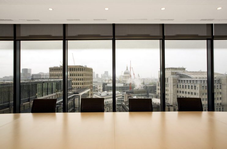 Modern boardroom setup with large conference table, executive chairs, and digital presentation screen in a corporate offic...