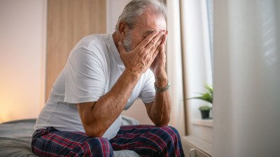 Elderly man with a concerned expression sitting at a desk, symbolizing anxiety and contemplation in aging or financial mat...