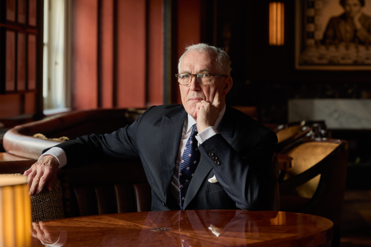 Breaking news event with journalists gathered at a press conference, microphones on a podium, and a large crowd in attendance