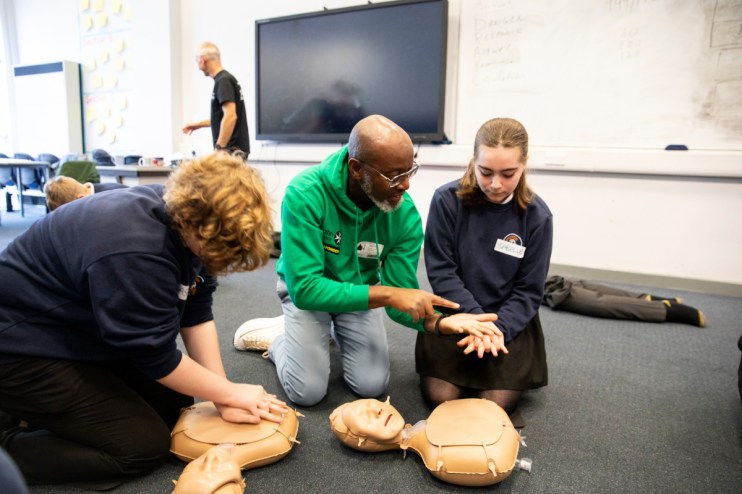 Young St. John Ambulance responders practicing first aid skills, wearing uniforms, engaging in hands-on emergency training.