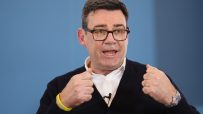 Andy Burnham speaking at a public event, wearing a suit, addressing an audience with a focused expression and engaged deme...