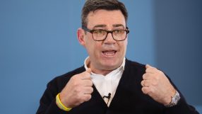 Andy Burnham speaking at a public event, wearing a suit, addressing an audience with a focused expression and engaged deme...