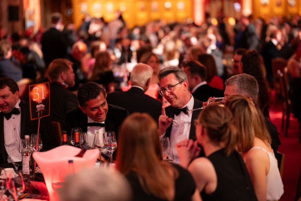 City AM Awards atmosphere with elegant gala setting, attendees in formal attire, glittering lights, and award stage in the...