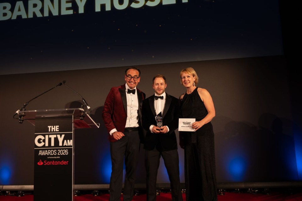 Barney receiving award at City AM Awards ceremony, surrounded by applauding attendees in formal attire