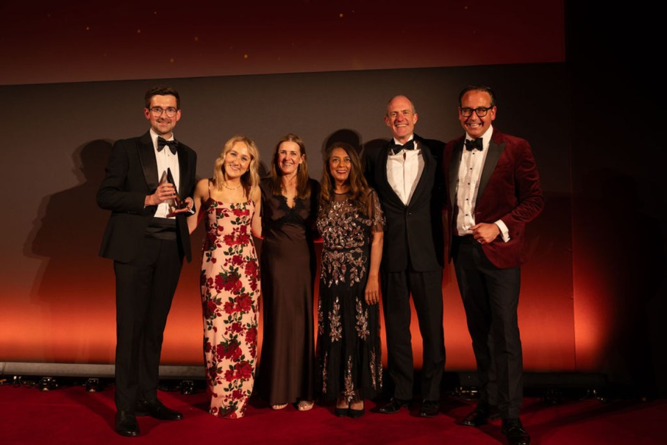 Shawbrook Bank celebrates win at City AM Awards with team on stage holding trophy in formal attire