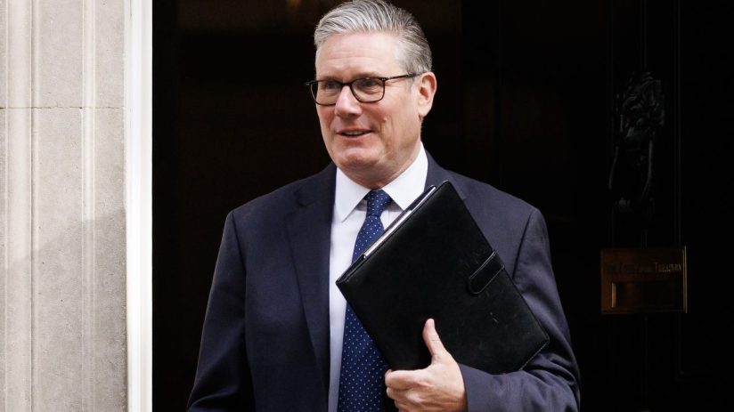 Keir Starmer speaking at a podium, addressing an audience in a formal setting, wearing a suit and tie, in a news conference