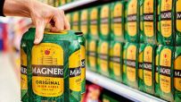 Magners cider bottles displayed on a wooden table with fresh apples and a scenic orchard in the background.