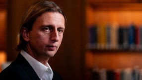 Revolut CEO Nik Storonsky speaking at a business conference, wearing a suit and tie, addressing financial innovation.