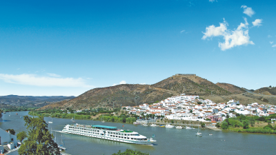 Luxury cruise ship docked at a sunny Spanish port, surrounded by clear blue waters and scenic coastal views.