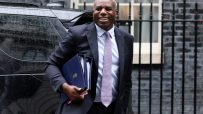 David Lammy speaking at a podium during a press conference, wearing a suit and addressing the audience with a serious expr...