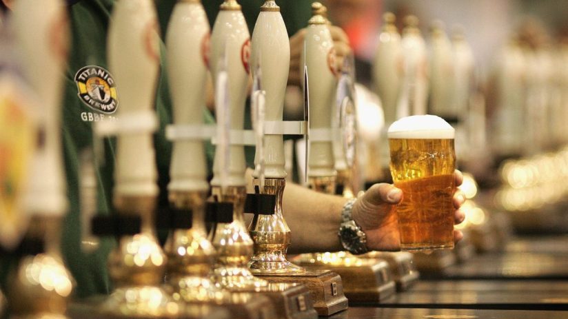 A full pint of beer with frothy head on a wooden bar counter, illuminated by soft ambient lighting in a cozy pub setting