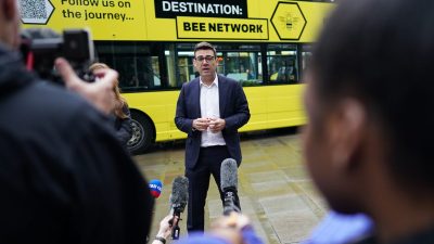 Andy Burnham discussing Bee Network devolution plan with city skyline in background