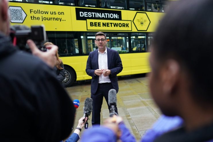 Andy Burnham discussing Bee Network devolution plan with city skyline in background