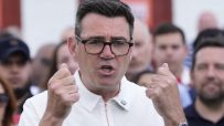 Andy Burnham delivering a speech at a public event, wearing a suit and tie, addressing an audience with a serious expression.