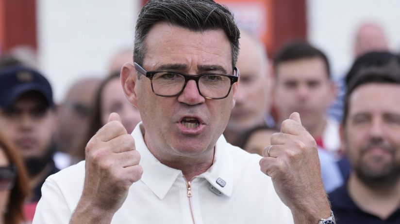 Andy Burnham delivering a speech at a public event, wearing a suit and tie, addressing an audience with a serious expression.