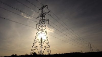 Electricity grid infrastructure with high-voltage power lines and pylons under a clear sky, representing energy distribution.