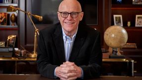 John Caudwell in a formal setting, possibly during a business meeting or public speaking event, conveying professionalism.