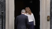 Keir Starmer standing near Number 10 Downing Street discussing political matters with media presence in the background