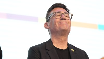 Andy Burnham smiling at a public event, wearing a suit and tie, representing positive leadership and community engagement.