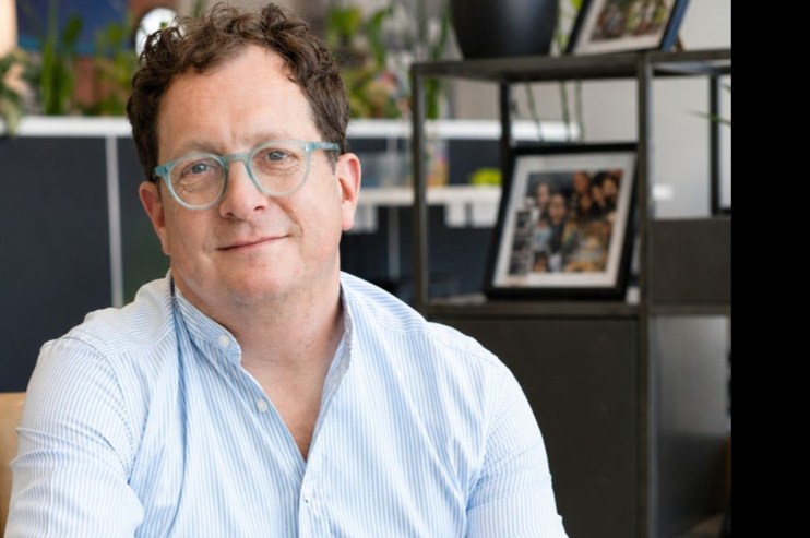 Smiling man with light blue glasses and striped shirt in an office setting.