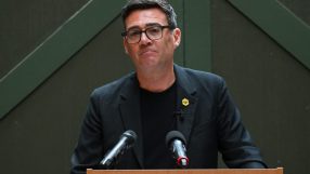 Andy Burnham speaking at a press conference, addressing current events and regional developments, wearing a suit and tie.