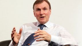 Archie Norman, business leader, speaking at a corporate event wearing a suit and tie, engaging with the audience.