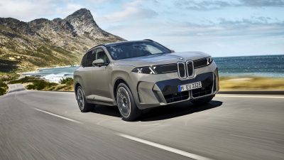 BMW X5 driving on a coastal road with mountains and ocean in the background, showcasing its sleek design.