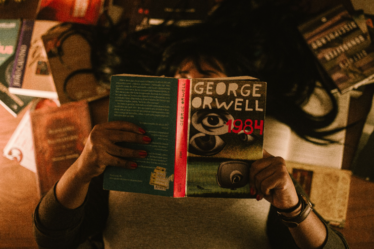 Stack of popular dystopian novels including 1984 and Brave New World on a wooden table, perfect for book enthusiasts.