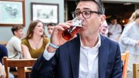 Andy Burnham, Mayor of Greater Manchester, drinks a pint of ale in a pub with people blurred in the background