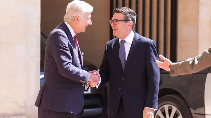 Two business professionals shaking hands outside a building, engaging in a formal meeting.