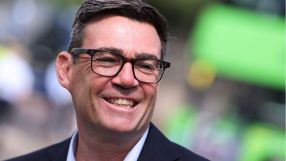 Andy Burnham, Mayor of Greater Manchester, smiling in glasses, dark jacket, light blue shirt, blurred green background.