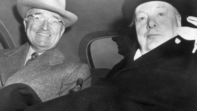 Harry Truman, smiling in a fedora, and Winston Churchill in a bowler hat, seated together in a car.